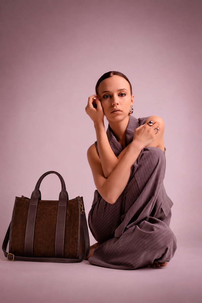 Model seated beside a brown suede tote